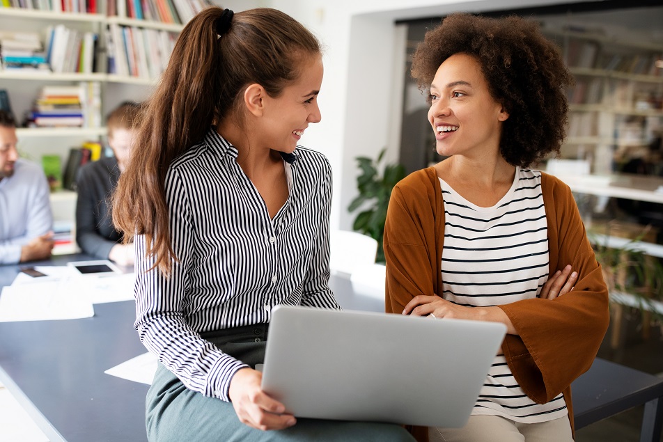 two business women talking by a laptop computer