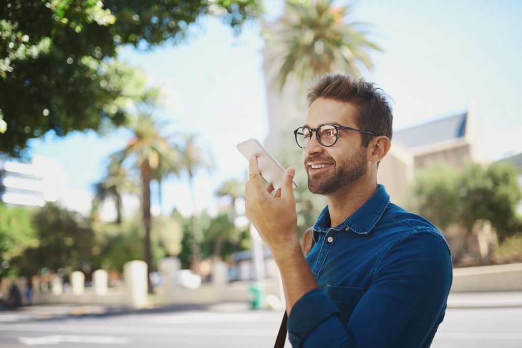 Happy man, city or talking with speaker phone for communication, audio message or voice note. Young, male person or tourist with smile on mobile smartphone for sound recording or app in an urban town